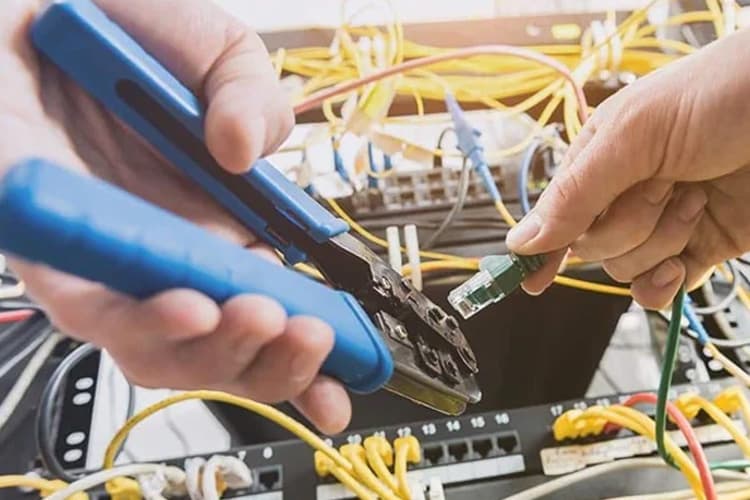 Eine Person arbeitet mit einer Zange an Datenkabeln.