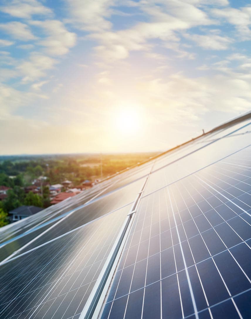 PV-Module auf einem Dach, das von der Sonne bei blauem Himmel beschienen wird, im Hintergrund Landschaft mit Siedlung