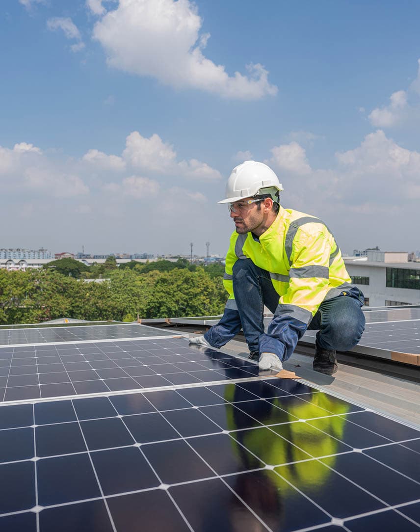 Ein Techniker in gelber Warnweste arbeitet an PV-Modulen auf einem Dach.
