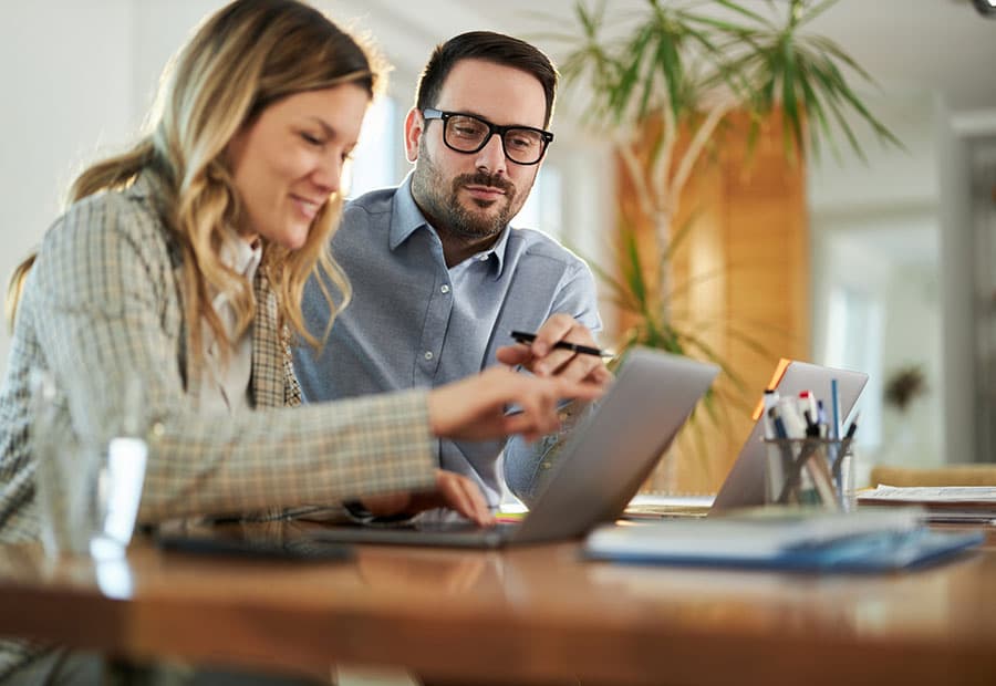 Eine Frau und ein Mann unterhalten sich über etwas auf einem Laptop auf einem Tisch.