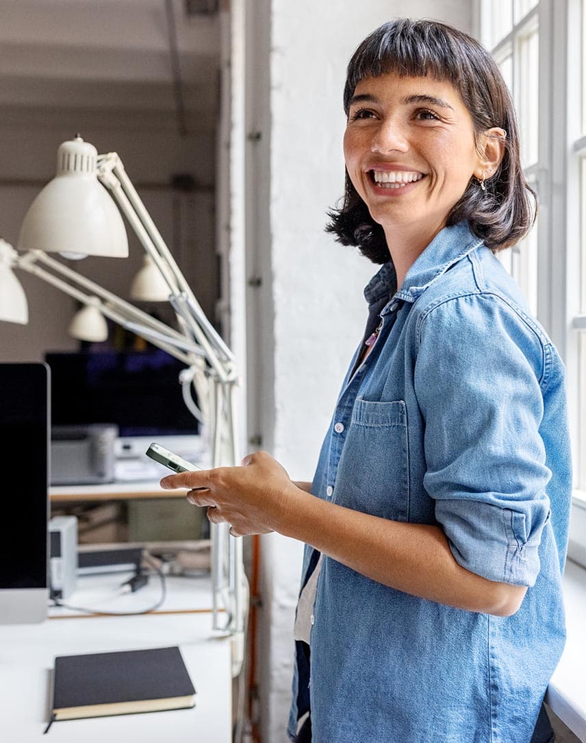 Eine lächelnde Frau steht in einem Büro neben einem Fenster.