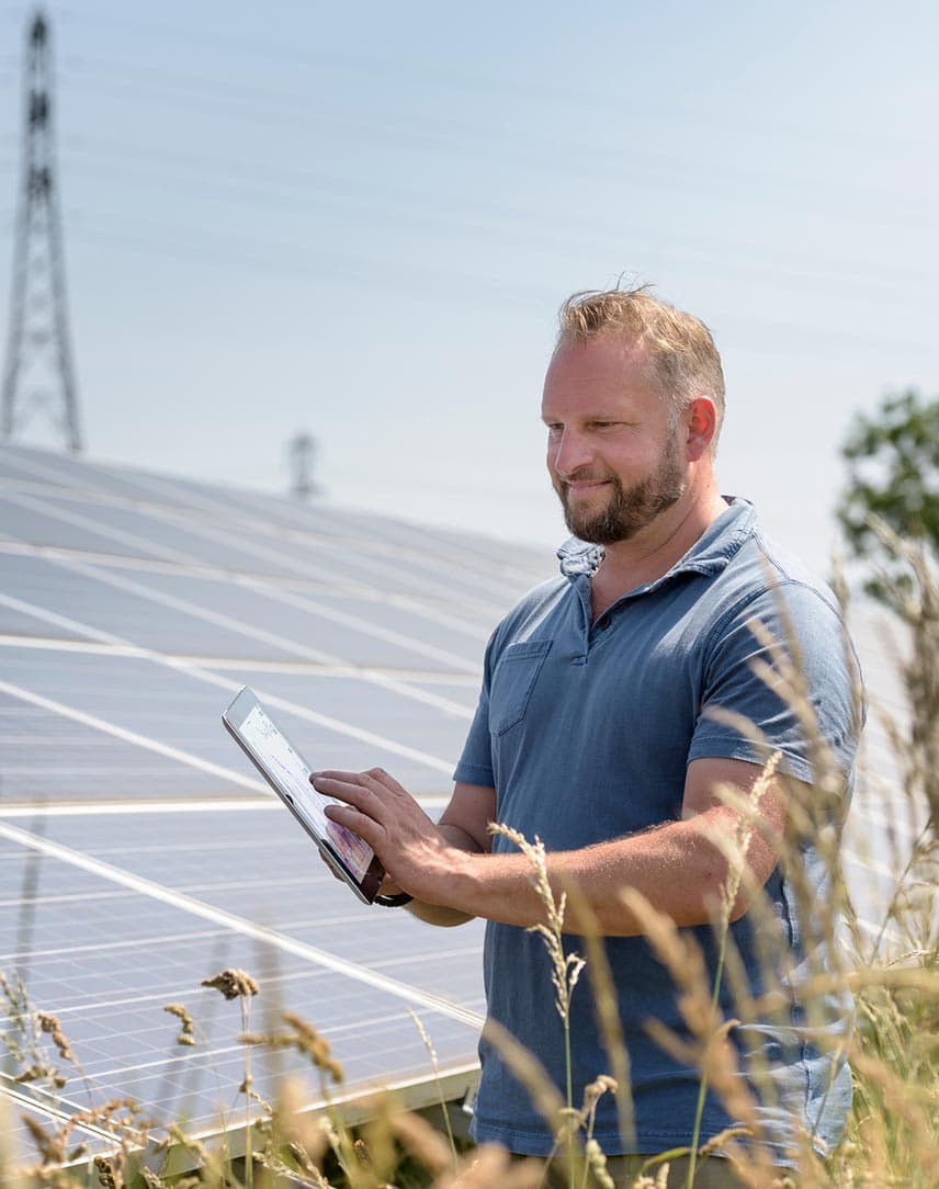Ein Mann mit Tablet vor einer PV-Freiflächenanlage