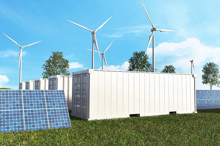 Mehrere Batteriespeicher-Container, daneben und dahinter PV-Anlagen und Windräder
