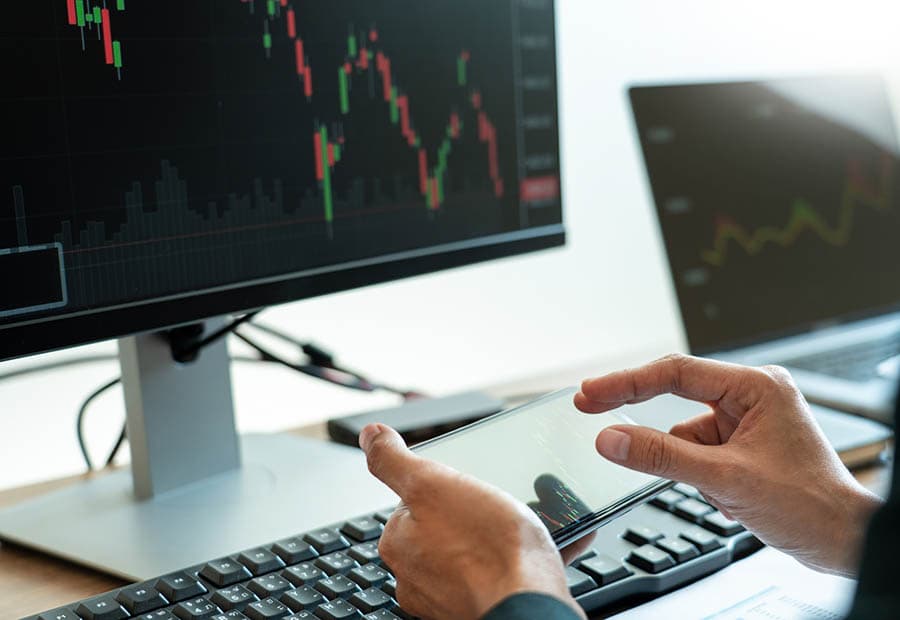 Börsenkürse auf Bildschirmen und Mobilgerät, das von einer Person bedient wird