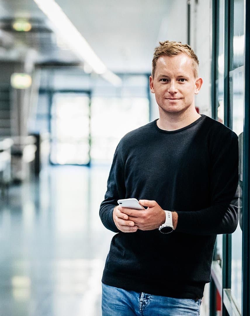 Ein Mann mit Kaffeebecher, der in einem Büro an einer Glasfront lehnt