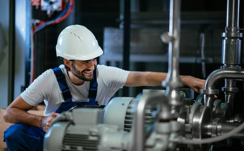 Ein Techniker in Blaumann mit weißem Helm arbeitet an einem Aggregat.
