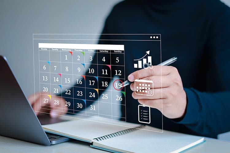 Eine Person im dunklen Pullover vor einem Holo-Kalender über einem Laptop