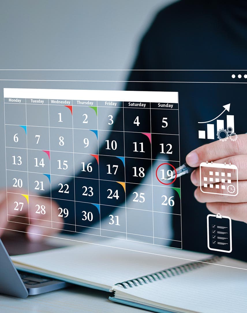 Eine Person im dunklen Pullover vor einem Holo-Kalender über einem Laptop