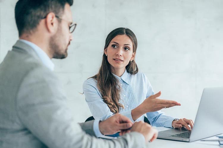 Eine Frau erklärt einem Mann etwas auf einem Laptop und weist auf diesen.