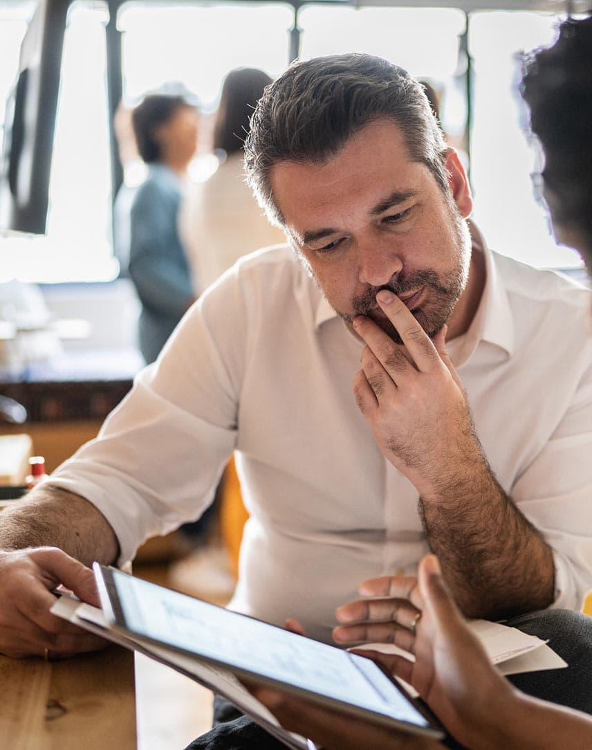 Ein Mann guckt auf ein Tablet, auf dem eine Frau ihm etwas erläutert.