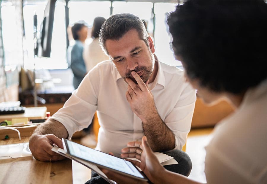 Ein Mann guckt auf ein Tablet, auf dem eine Frau ihm etwas erläutert.