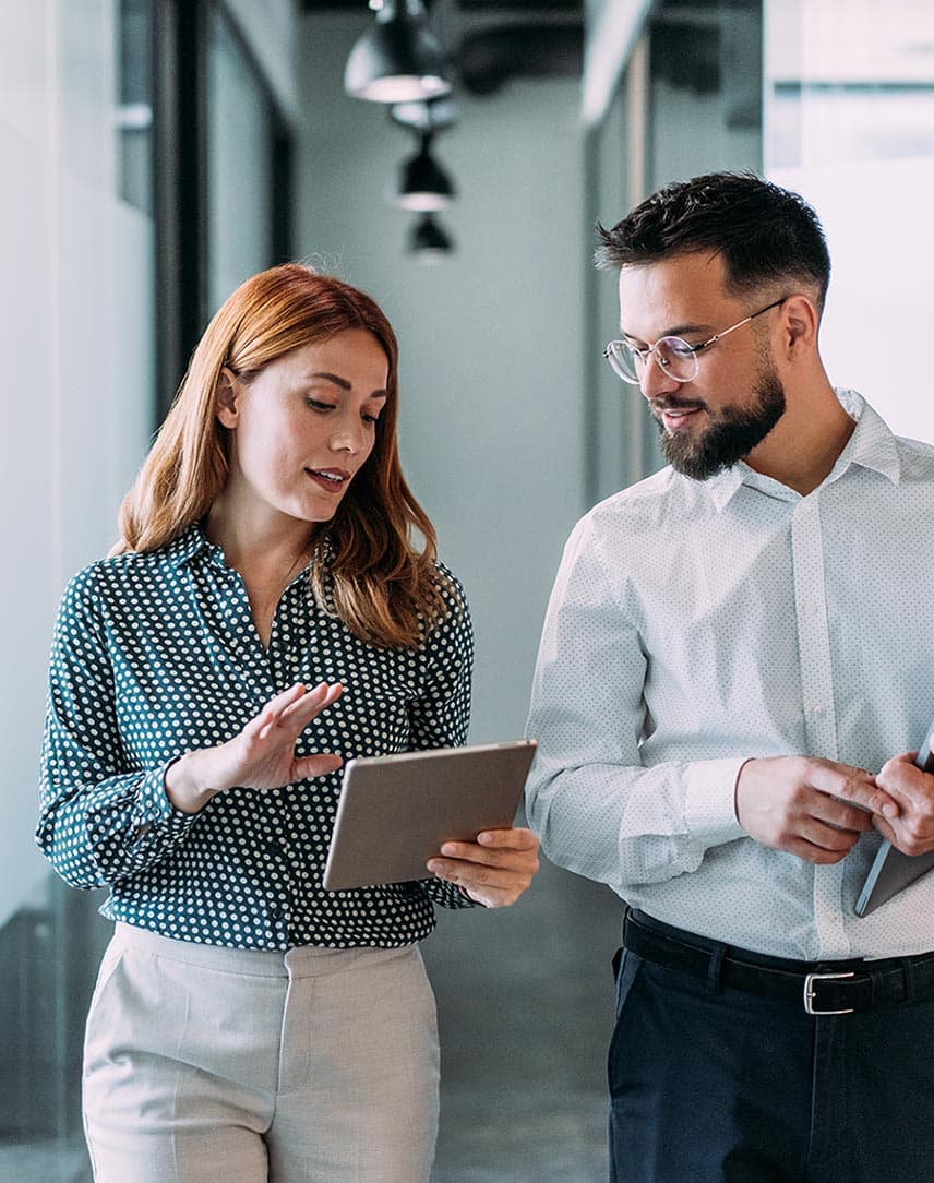 Eine Frau zeigt einem Kollegen im Laufen etwas auf einem Tablet.