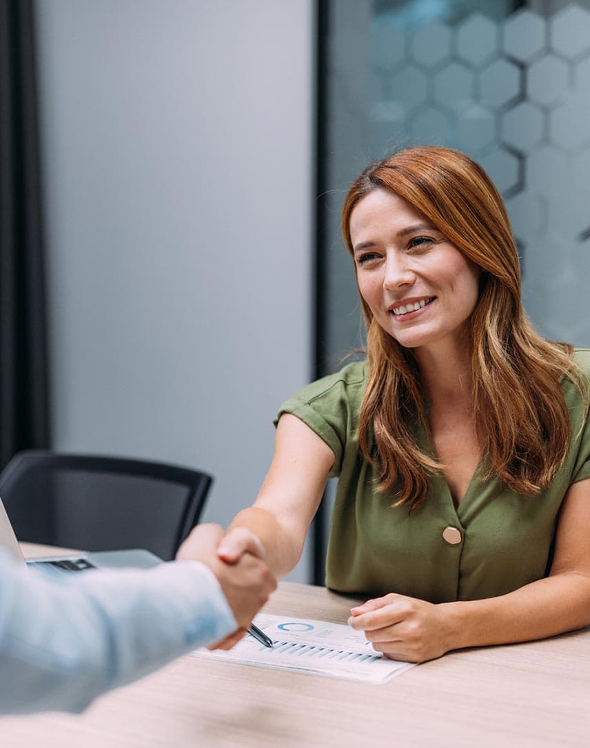 Eine Frau sitzt an einem Meetingtisch und reicht ihrem Kollegen die Hand.