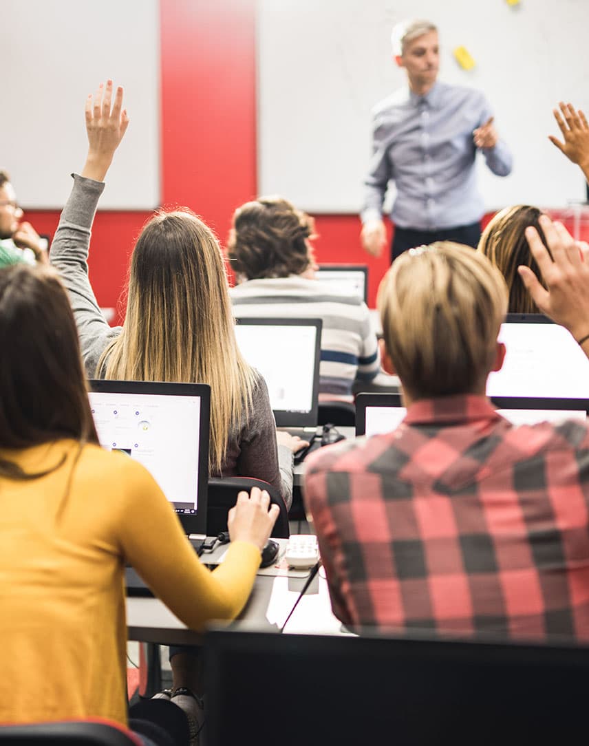 In einem Klassenzimmer sitzen jugendliche Schülerinnen und Schüler an Laptops.