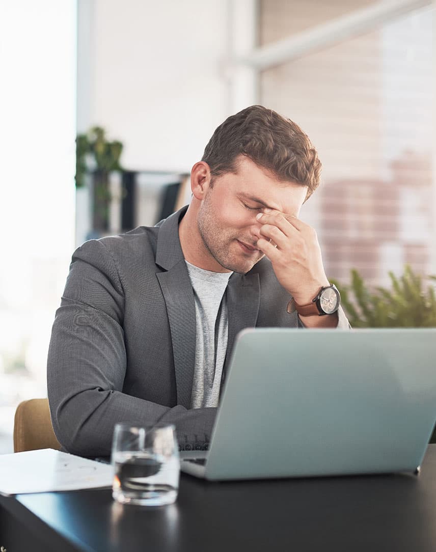 Ein Mann sitzt vor seinem Bürorechner und stützt sein Gesicht betroffen mit der Hand.