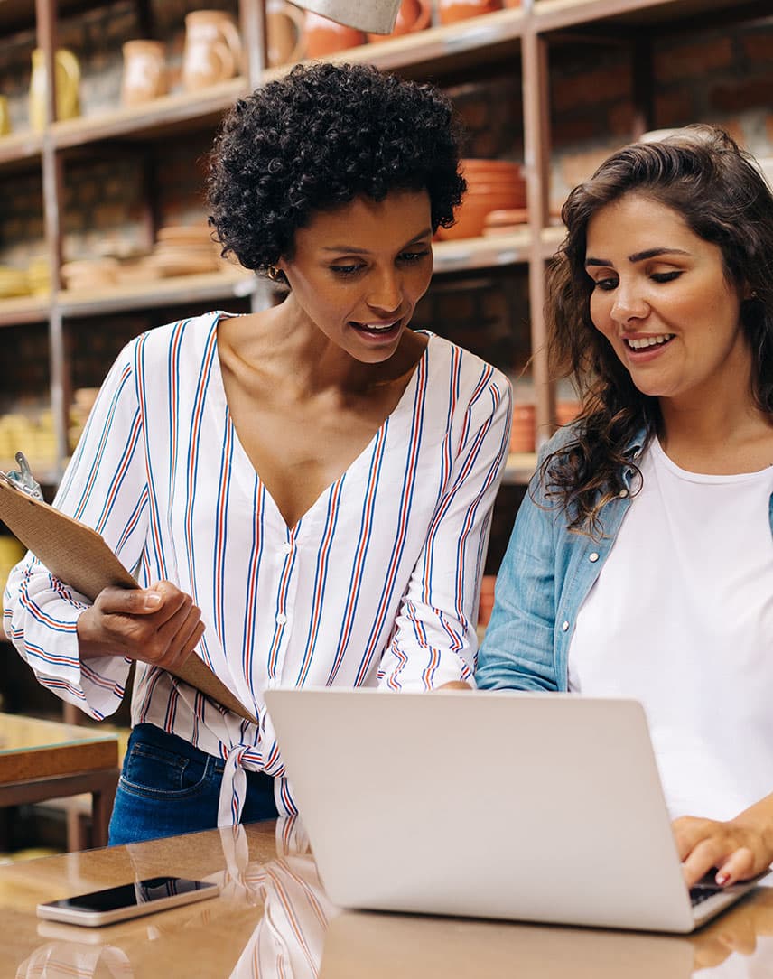 Zwei junge Ladenbesitzerinnen gucken an der Ladentheke auf ein Notebook und freuen sich