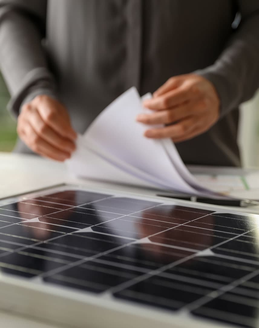 Ein Mann blättert in Formularen, im Vordergrund ein PV-Modul