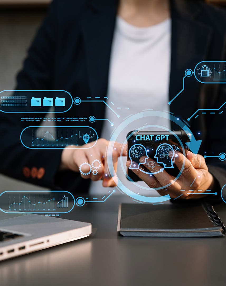 Eine Frau im schwarzen Blazer sitzt vor einem Laptop, im Vordergrund hellblau stilisierte Symbole für Künstliche Intelligenz