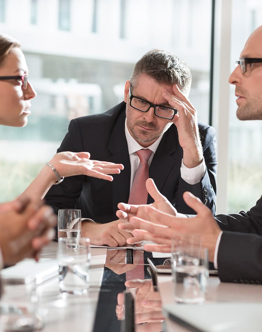 Geschäftsleute sitzen an einem Tisch. Sie diskutieren miteinander. Am Kopf des Tisches sitzt der Chef und grübelt nach.