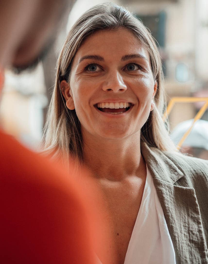 Eine lächelnde Frau und ein Mann von hinten in einem Geschäft, dahinter ein Schaufensterscheibe, die gerade gereinigt wird.