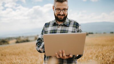 Ein Mann, der in einem Feld steht, liest etwas auf einem Notebook 