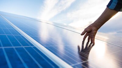 Ein Hand streicht über sonnenbeschienene PV-Module