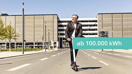 Ein Mann im Anzug auf einem E-Roller vor einem Industriegebäude