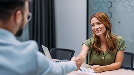Eine lächelnde Frau schüttelt einem Mann an einem Bürotisch die Hand.