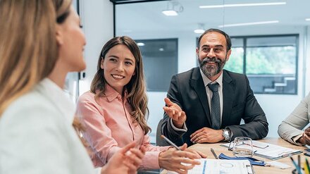 Zwei Frauen und ein Mann unterhalten sich geschäftlich an einem Tisch.