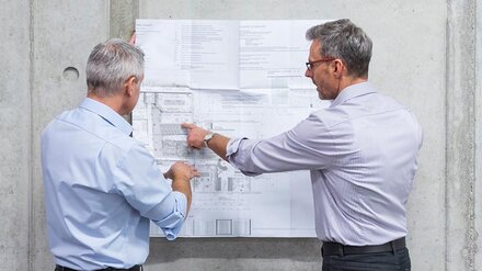 Zwei Männer besprechen einen Plan an der Wand