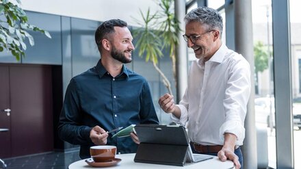 Zwei Männer unterhalten sich an einem Stehtisch in einem Unternehmen. 