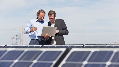Zwei Männer mit Laptop besprechen etwas an einer PV-Anlage.