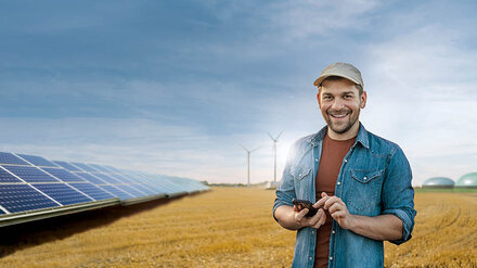 Ein junger Landwirt auf einem Feld, links eine PV-Anlage im Hintergrund Windräder und eine Biogasanlage