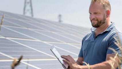 Ein Mann prüft etwas auf seinem Smartphone, daneben PV-Module