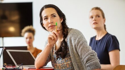 Sitzende dunkelhaarige Frau bringt sich in Workshop ein und zeigt mit Stift auf etwas