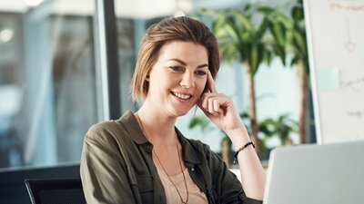 Eine Frau am Schreibtisch, die interessiert auf Ihren Arbeitsrechner guckt