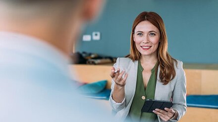 Eine Frau mit Sakko und Tablet erklärt einem Mann etwas.