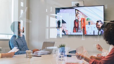 Mehrerer Menschen im Konferenzraum schauen auf einen Bildschirm während einer Videokonferenz