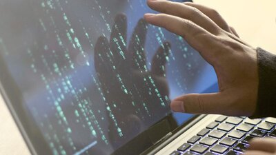 Hand eines stilisierten Hackers auf Laptop-Bildschirm