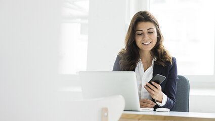 Frau mit Handy in der Hand vor dem Laptop