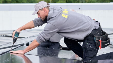 Ein Techniker mit EWE-Pullover installiert auf einem Firmendach PV-Module