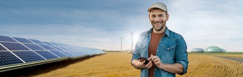Direktvermarktung mit EWE business Ein junger Landwirt auf einem Feld, links eine PV-Anlage im Hintergrund Windräder und eine Biogasanlage
