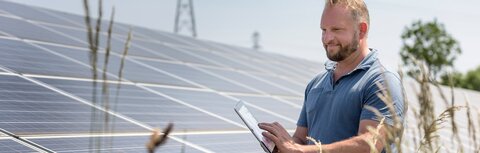Die EWE business App für Ihre Direktvermarktung Ein Mann prüft etwas auf seinem Smartphone, daneben PV-Module