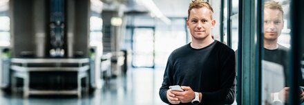 EWE business Terminmarktportal Ein Mann mit Handy, der in einem Büro an einer Glaswand lehnt