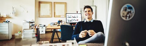 EWE business Extras Ein Mann an einem Schreibtisch zurückgelehnt im Stuhl und lachend