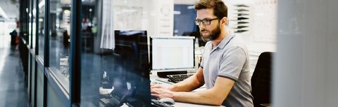 LAN-Lösungen von EWE Mann mit Brille in Großraumbüro am Computer