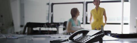 Fraud-TK-Anlagen von EWE Festnetztelefon im Vordergrund, zwei Frauen unscharf im Hintergrund
