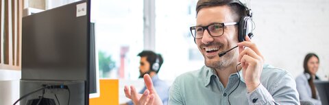 Telefonie von EWE Freundlicher Mann mit Headset vor einem Bildschirm