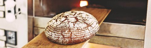 Bäckerei Heins Ein Brot, das auf einem Brett aus dem Ofen geholt wird