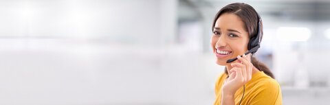 Jetzt Termin für telefonische Beratung mit EWE vereinbaren. Lächelnde Frau mit Headset und gelbem Oberteil
